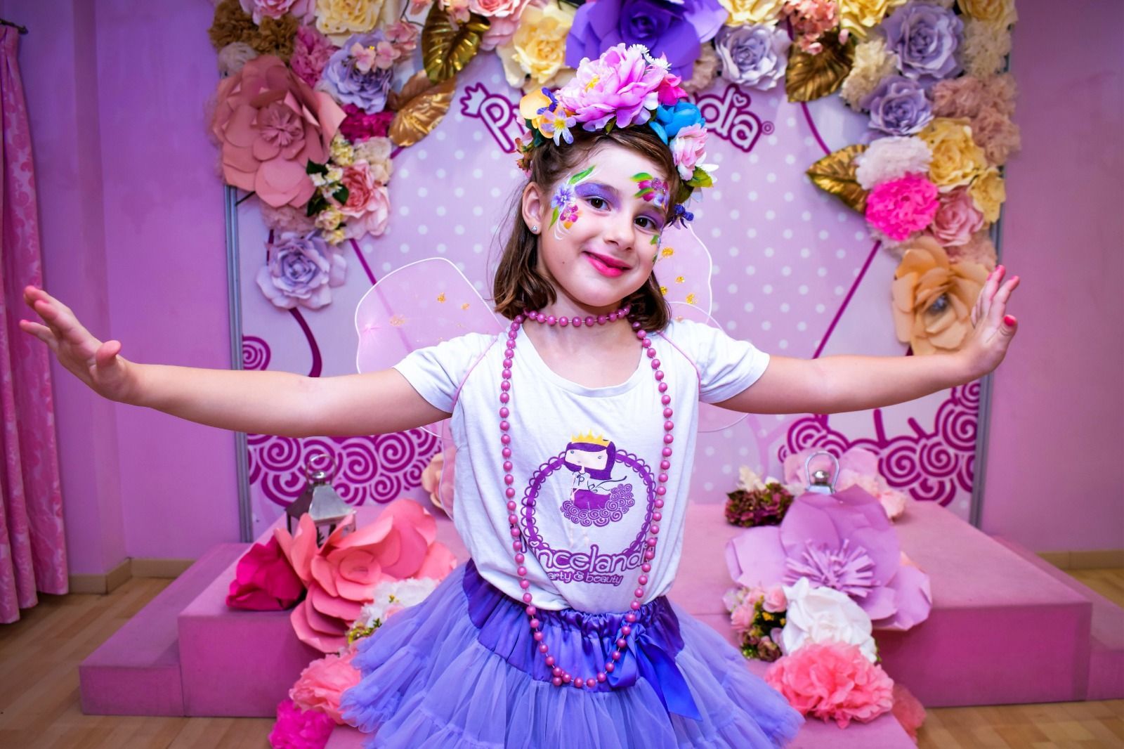Una niña con flores pintadas en la cara está parada frente a una pared de flores.