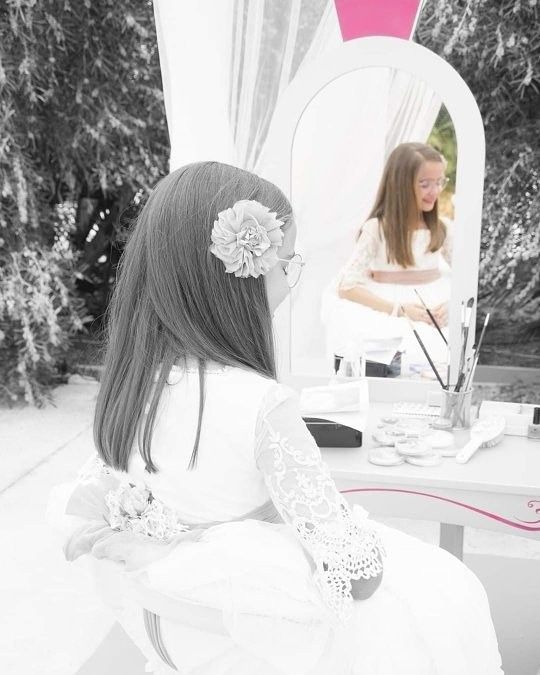 Una niña está sentada frente a un espejo con una flor en el pelo.