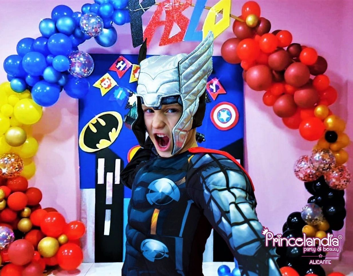 Un niño con un disfraz de Thor está parado frente a globos.