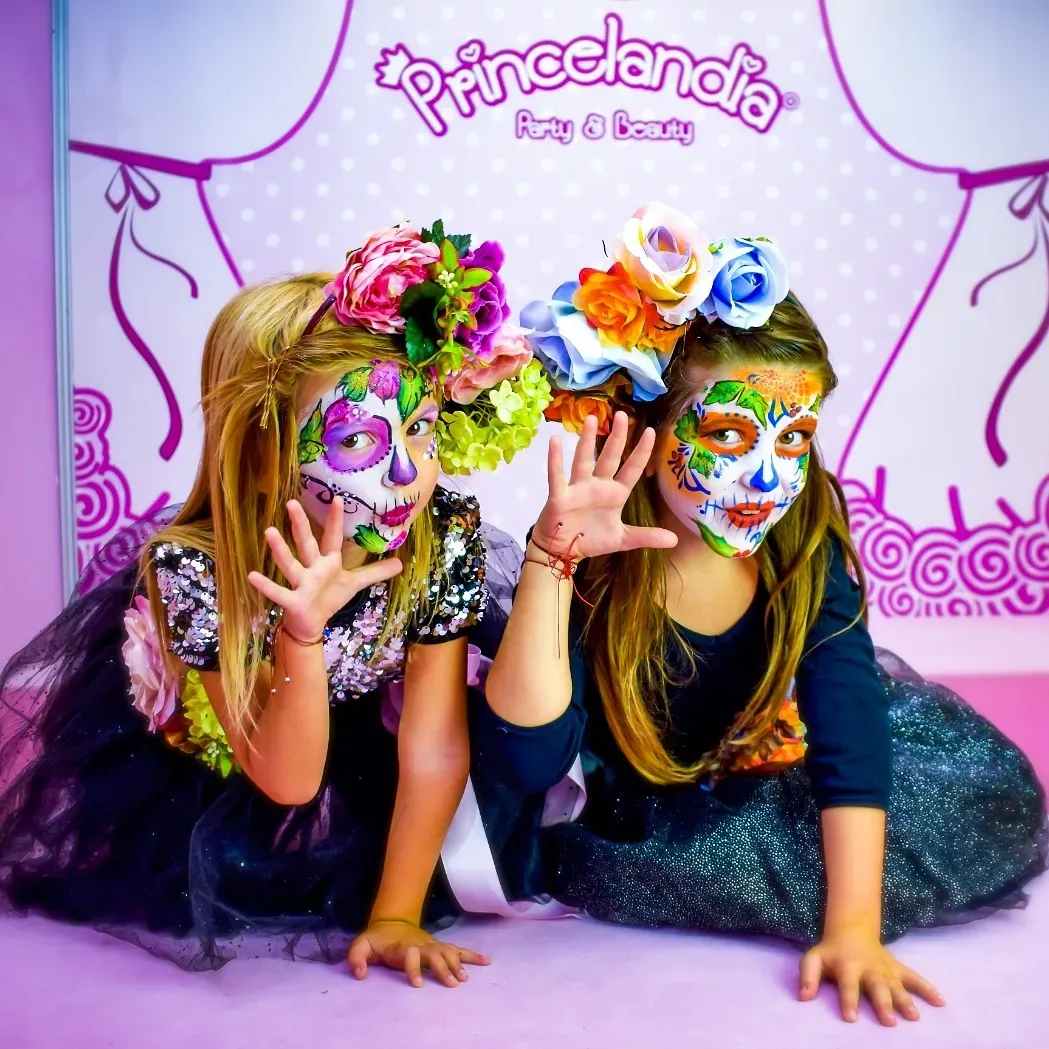 Dos chicas con pintura facial y flores en el pelo posan para una foto frente a un cartel que dice princelandia