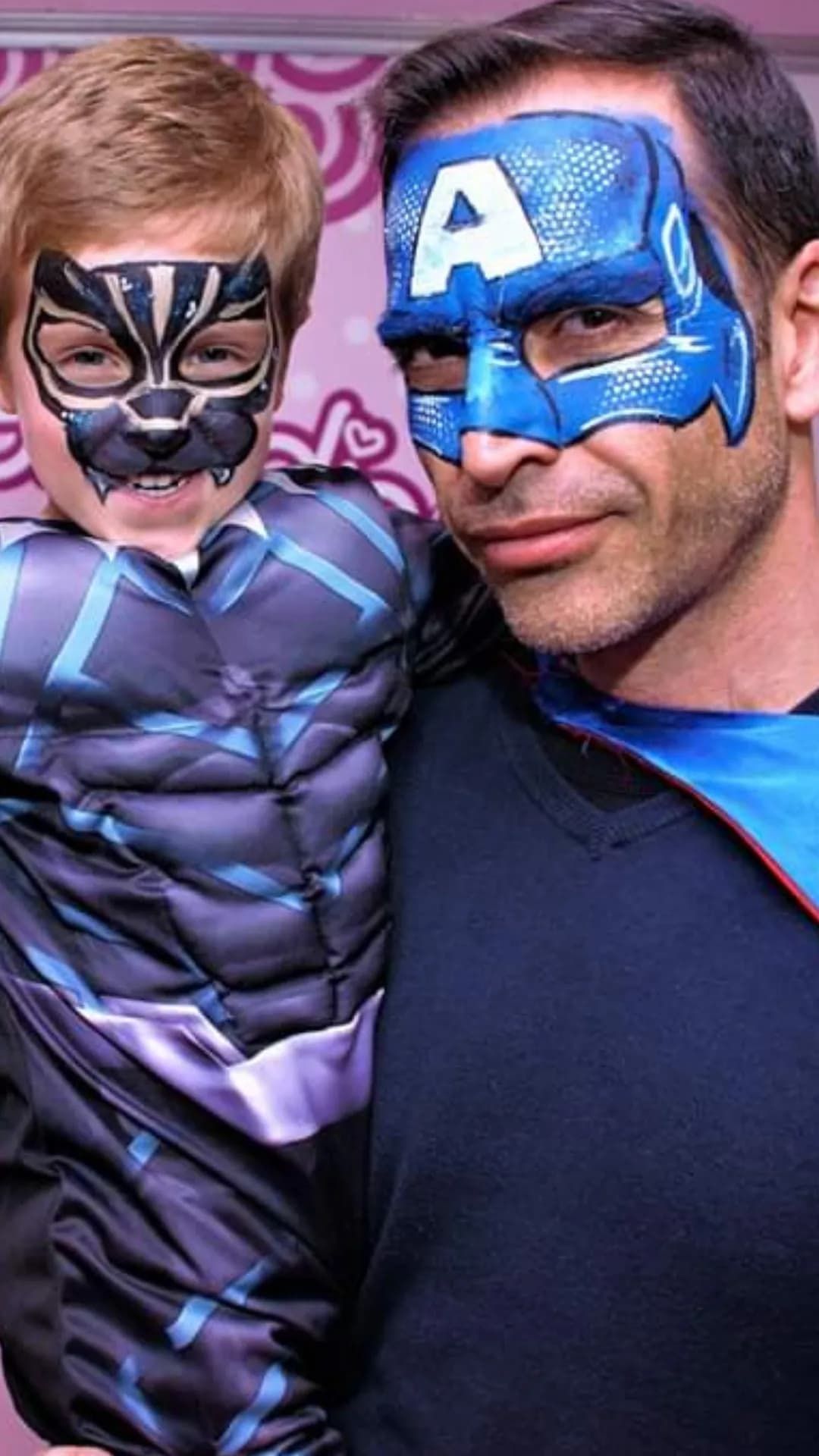 Un hombre sostiene a un niño pequeño con el Capitán América pintado en su cara.