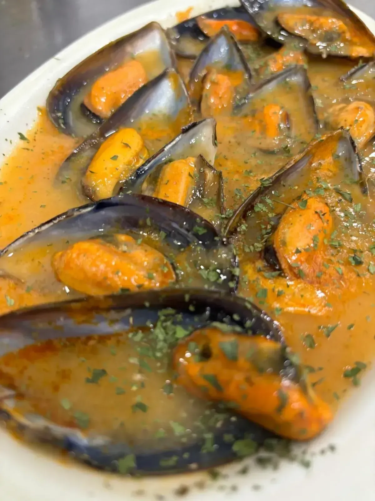 Mejillones en salsa cremosa de naranja con hierbas, servidos en un bol.
