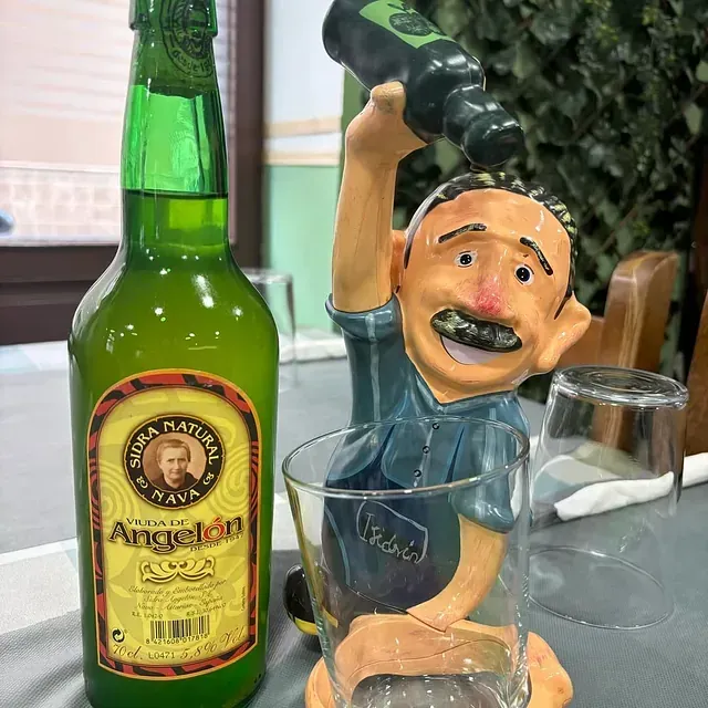 Una botella de cerveza Angelon junto a una figura de un hombre vertiéndola en un vaso.