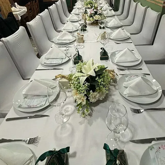 Una mesa larga con platos, servilletas, cubiertos y flores sobre ella.