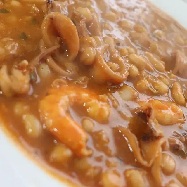 Un primer plano de un tazón de sopa con camarones y frijoles.