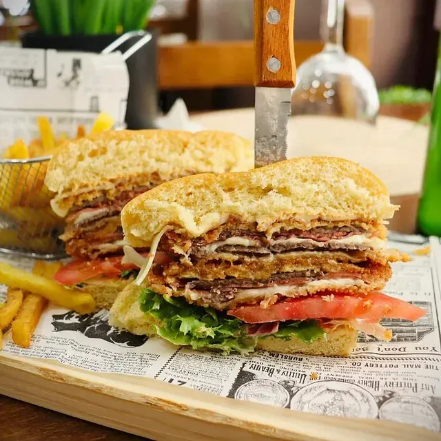 Dos sándwiches están sobre una tabla de cortar de madera encima de un periódico.