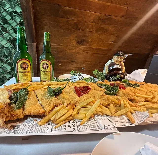 Un plato grande de comida con patatas fritas y dos botellas de cerveza en una mesa.