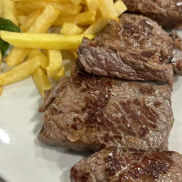 Un plato blanco cubierto con bistec y papas fritas