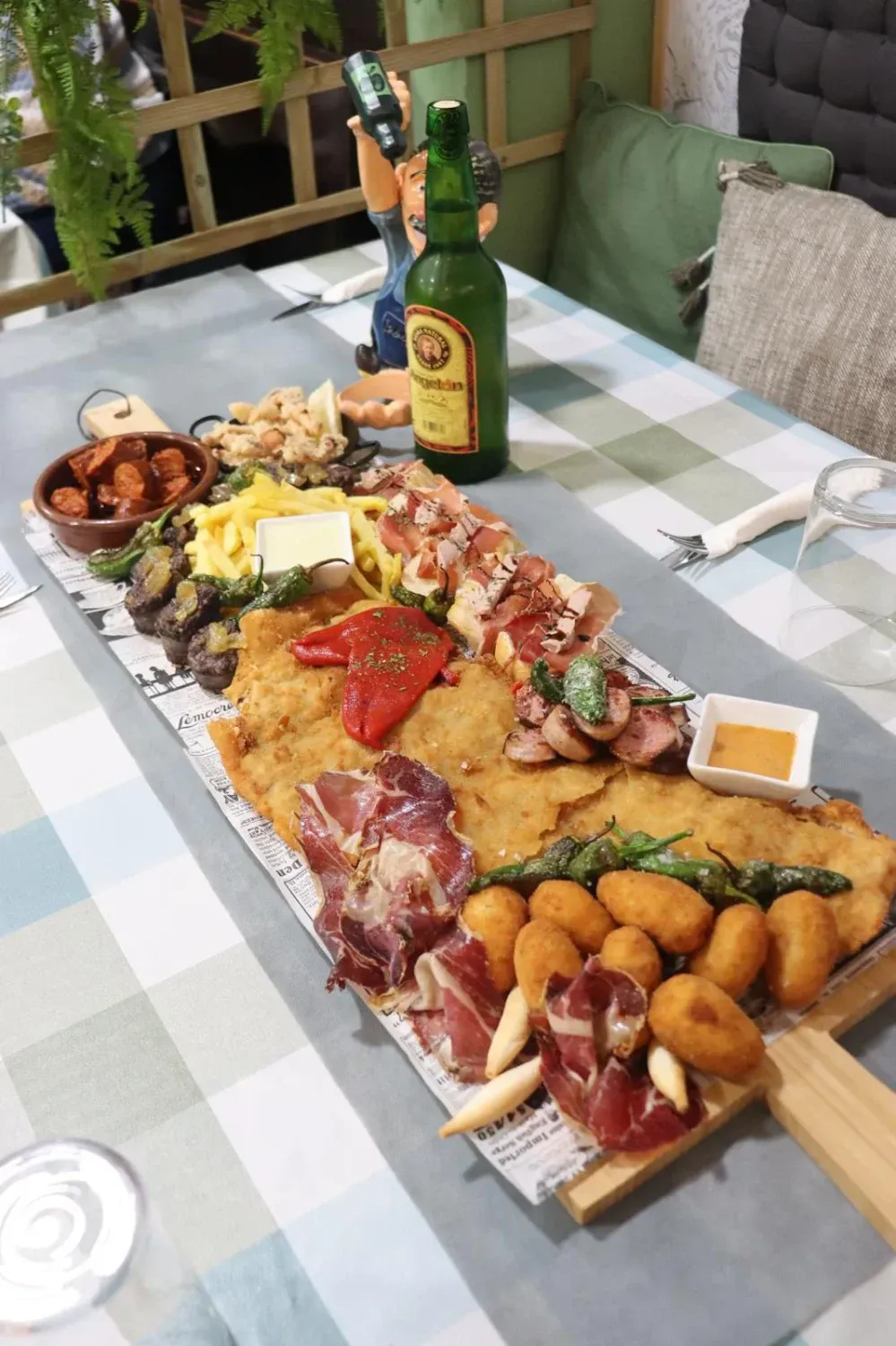 Tabla de embutidos con carnes variadas, quesos, croquetas y salsas sobre una mesa con una botella de aceite de oliva.