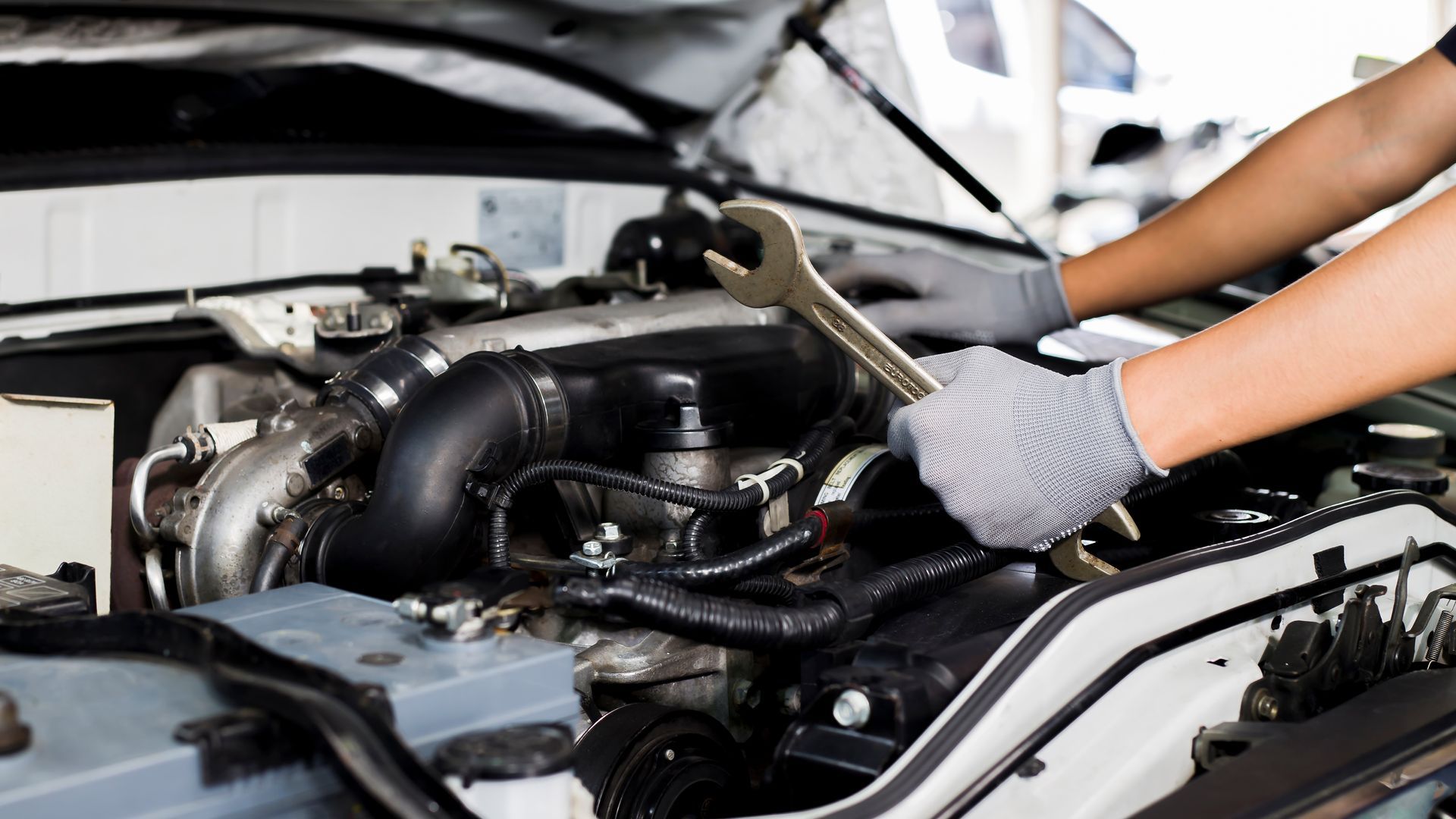 Mécanicien utilisant une clé pour travailler sur un moteur de voiture dans un garage.