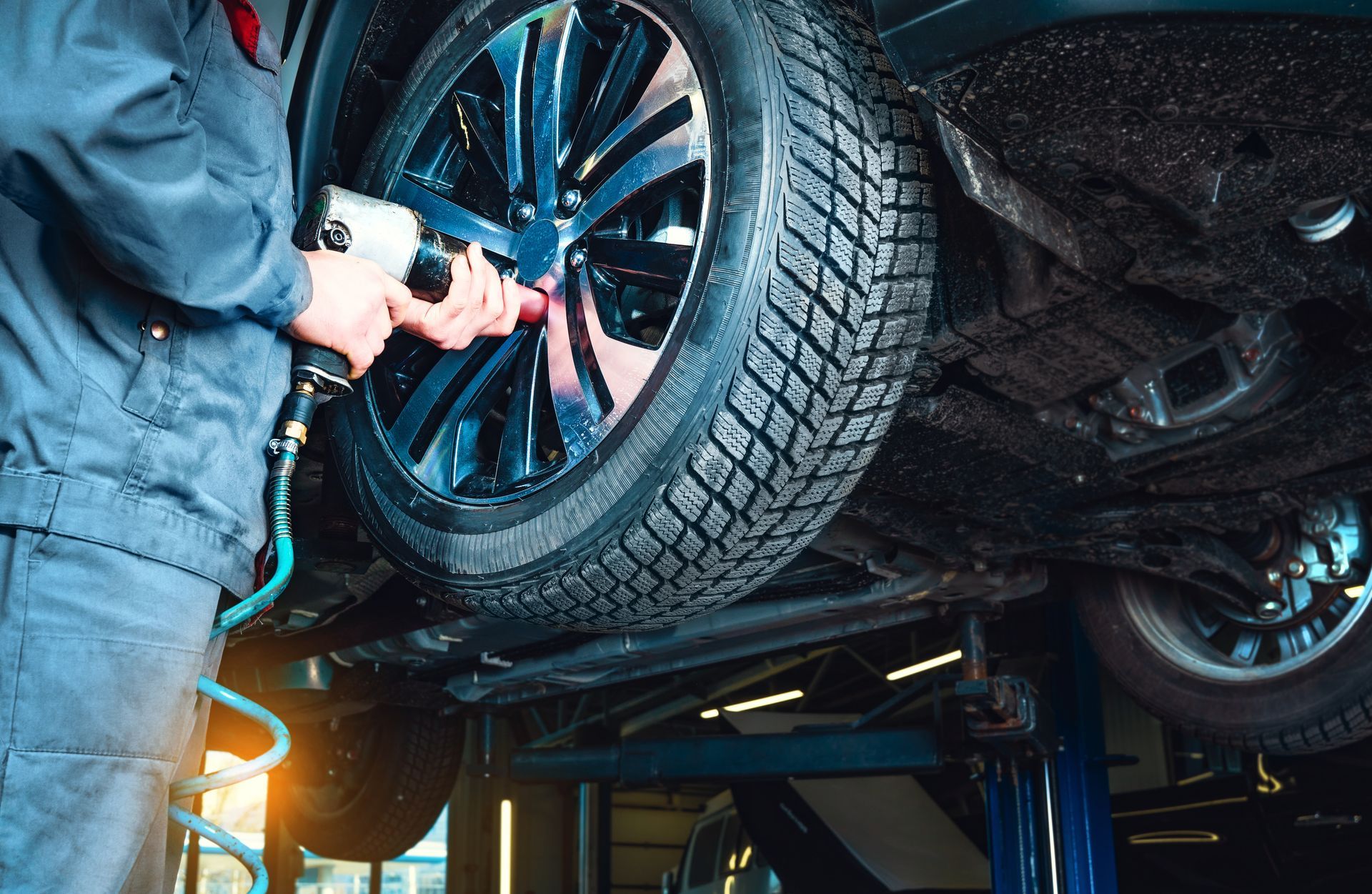 Mécanicien utilisant un outil électrique pour changer un pneu sur une voiture dans un garage.