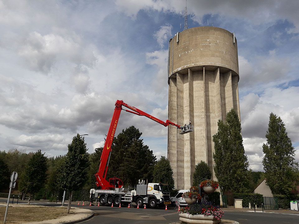 Grue sur poids lourd déployée devant un château d'eau
