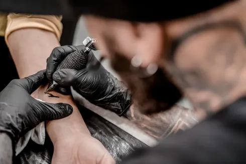 Un tatuador con guantes negros está tatuando una muñeca en un estudio.