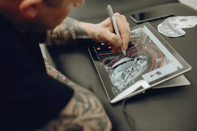 Persona con tatuajes dibujando en una tableta con un lápiz.