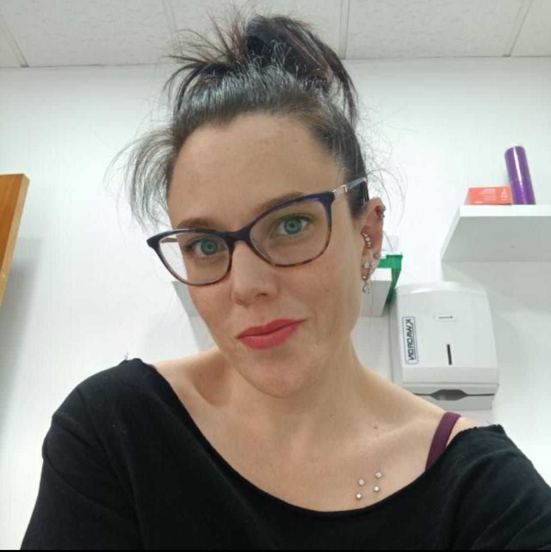 Mujer de cabello oscuro mirando a la cámara con una leve sonrisa. Al aire libre, con ramas de árboles al fondo.