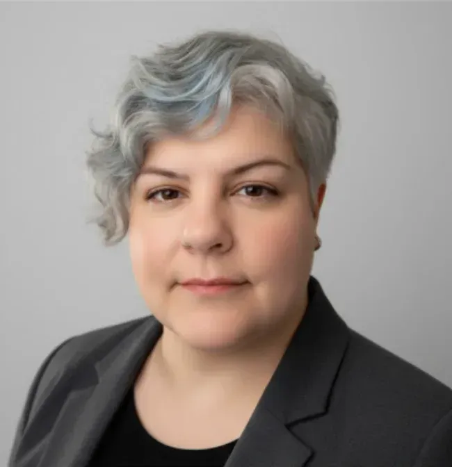 Mujer con cabello gris y ondulado y blazer gris.