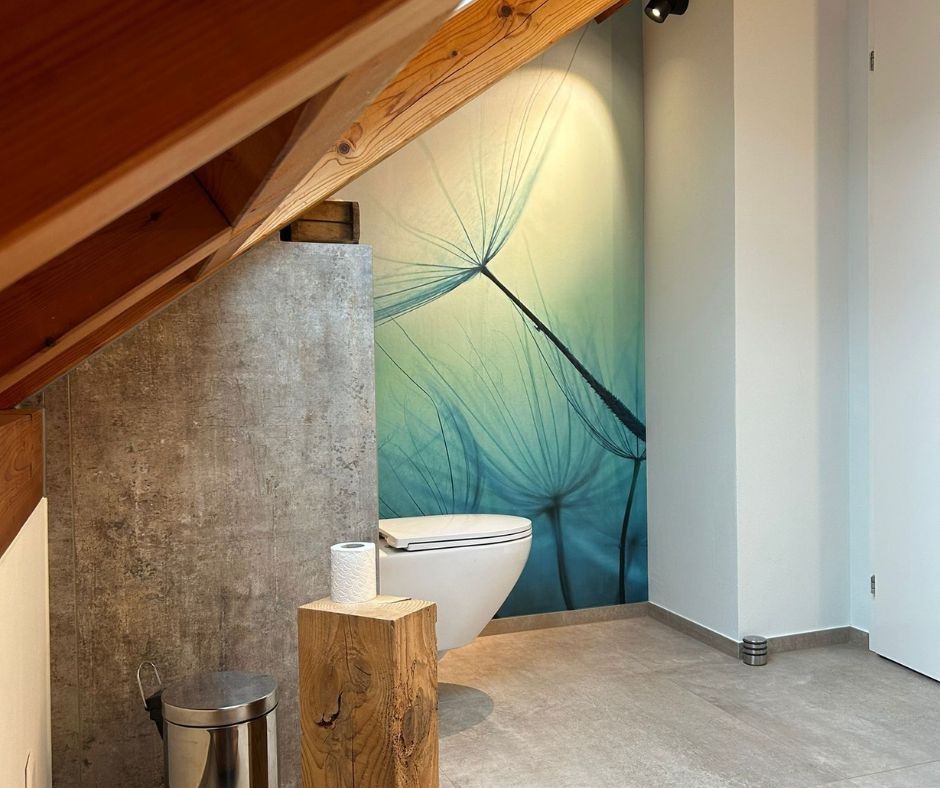 Toilette in einem dachbodenähnlichen Raum mit einem Löwenzahn-Wandgemälde, Betonsäule, Holzakzenten und hellen Holzböden.