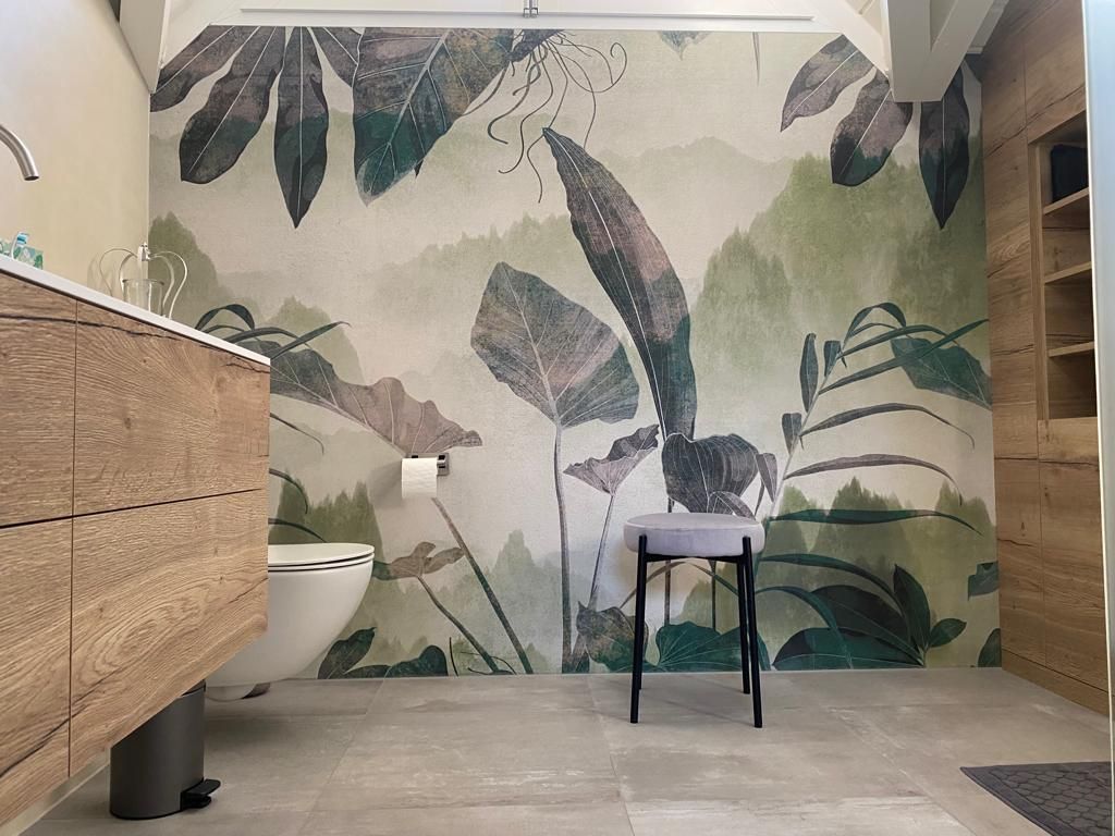 Badezimmer mit botanischem Wandgemälde, Holzwaschtisch, grauem Hocker und Toilette.