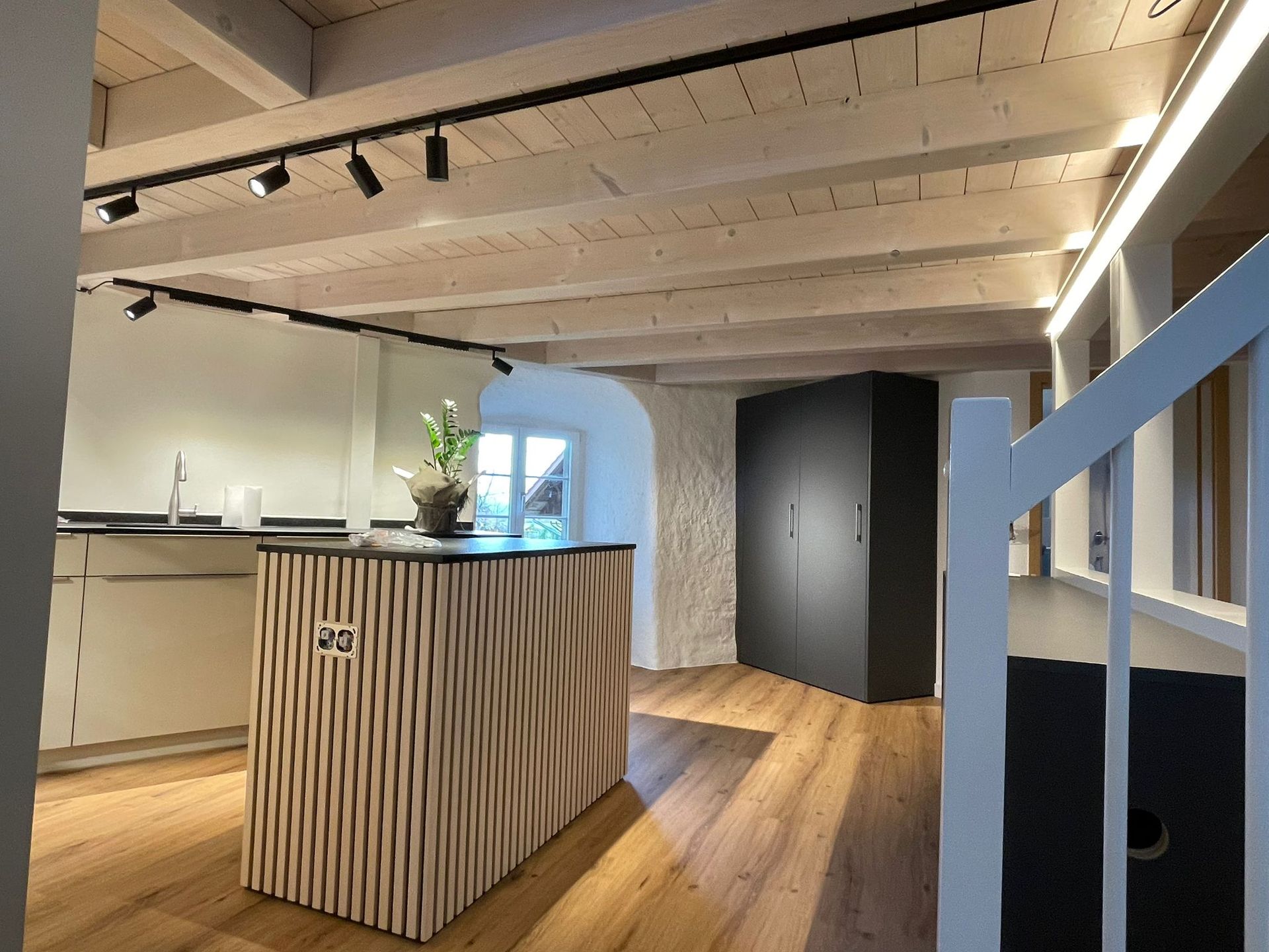 Moderne Küche mit Holzinsel, weißen Wänden, Holzbalken und einer Treppe.