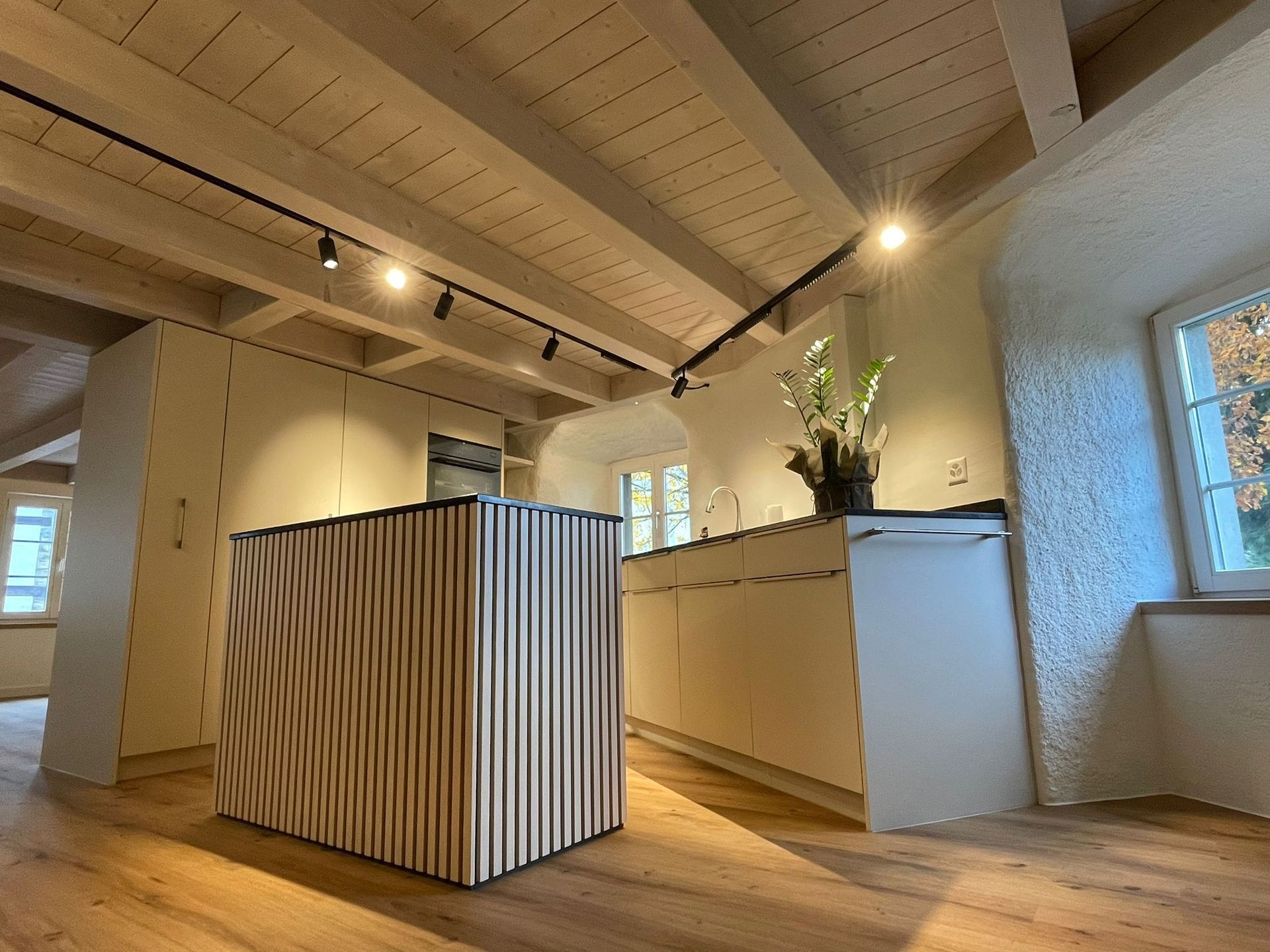 Moderne Küche mit hellen Holzbalken, Schränken und einer strukturierten Kochinsel.