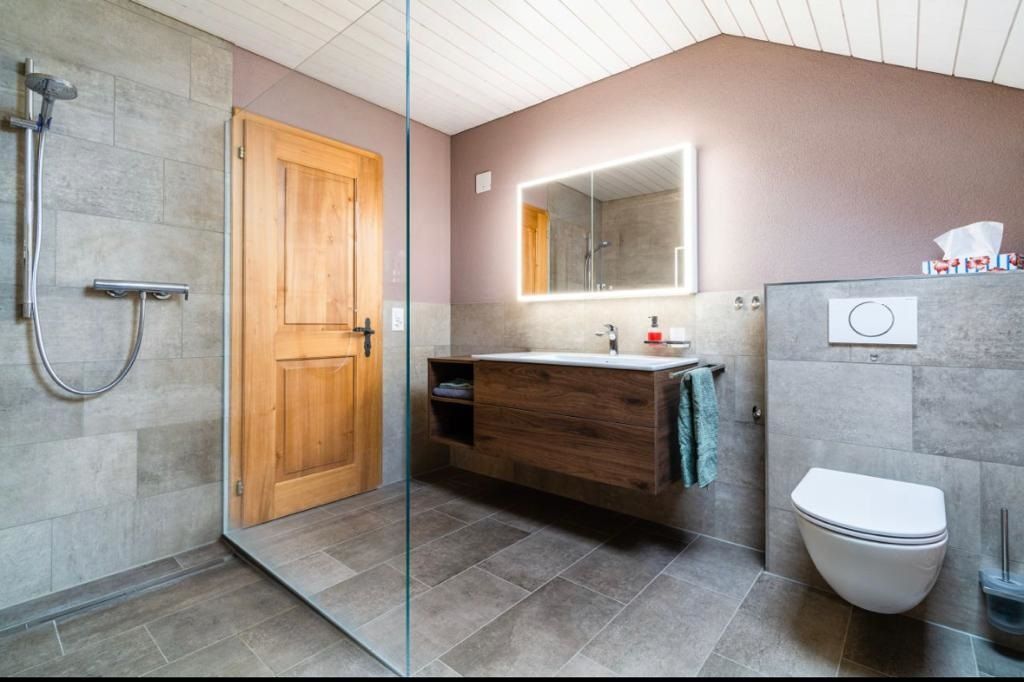 Badezimmer mit Dusche, Toilette, Holzwaschtisch und Steinfliesen.