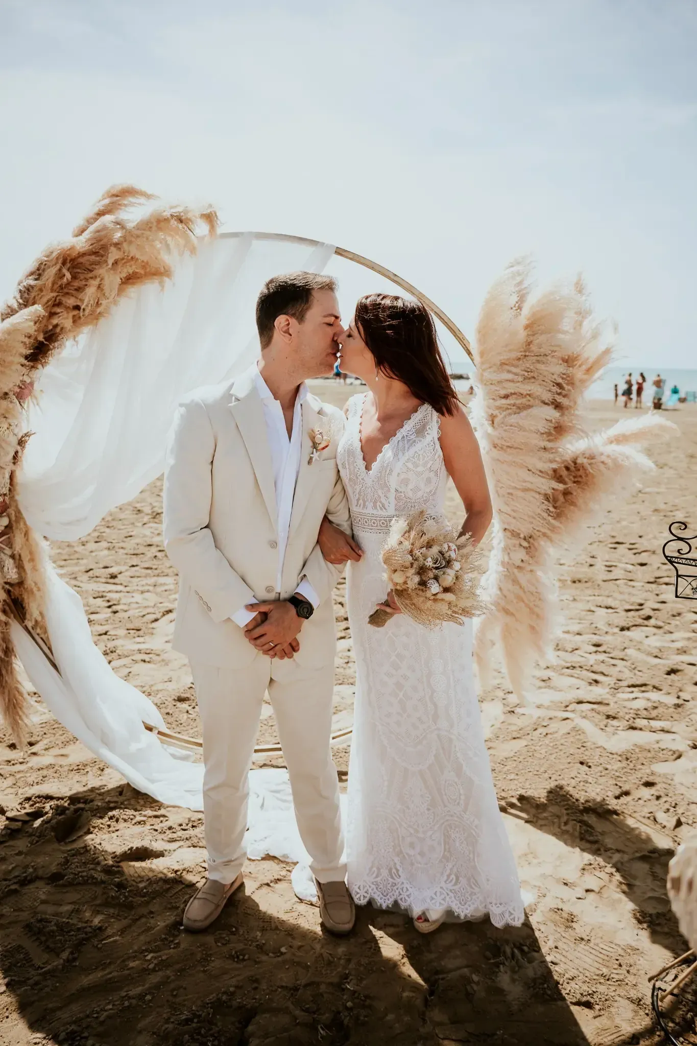 Pareja besándose en una ceremonia de boda en la playa, con arco de hierba de la pampa.