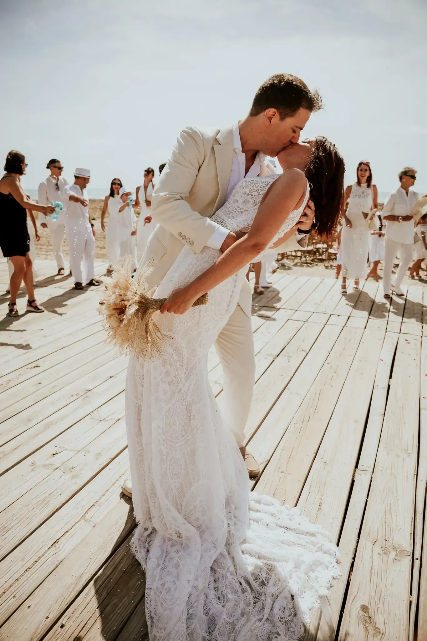 Pareja besándose en una pasarela de madera, ceremonia nupcial. La novia con vestido de encaje, el novio con traje blanco