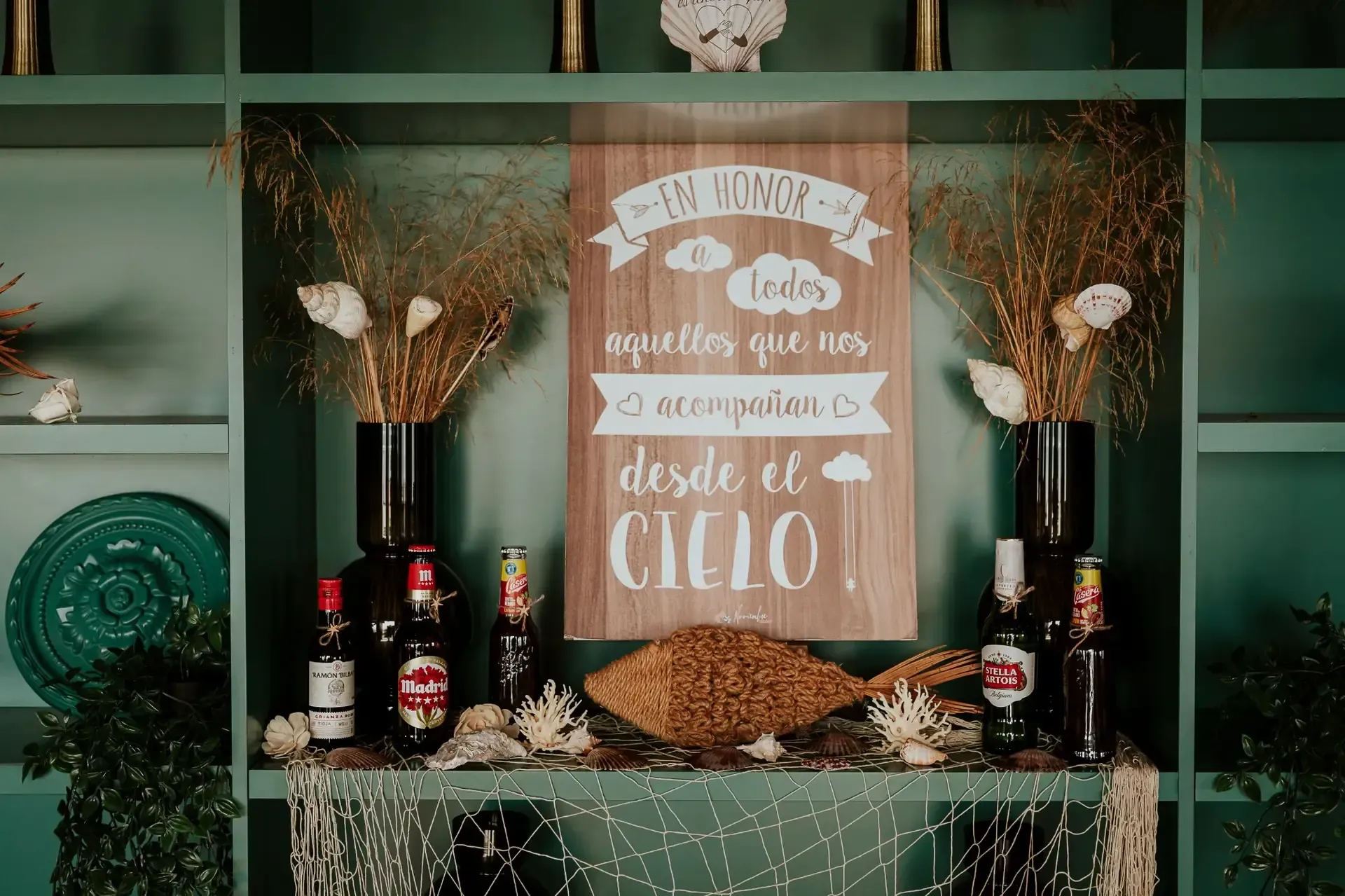 Estantería verde con adornos, botellas y un cartel de madera que dice 
