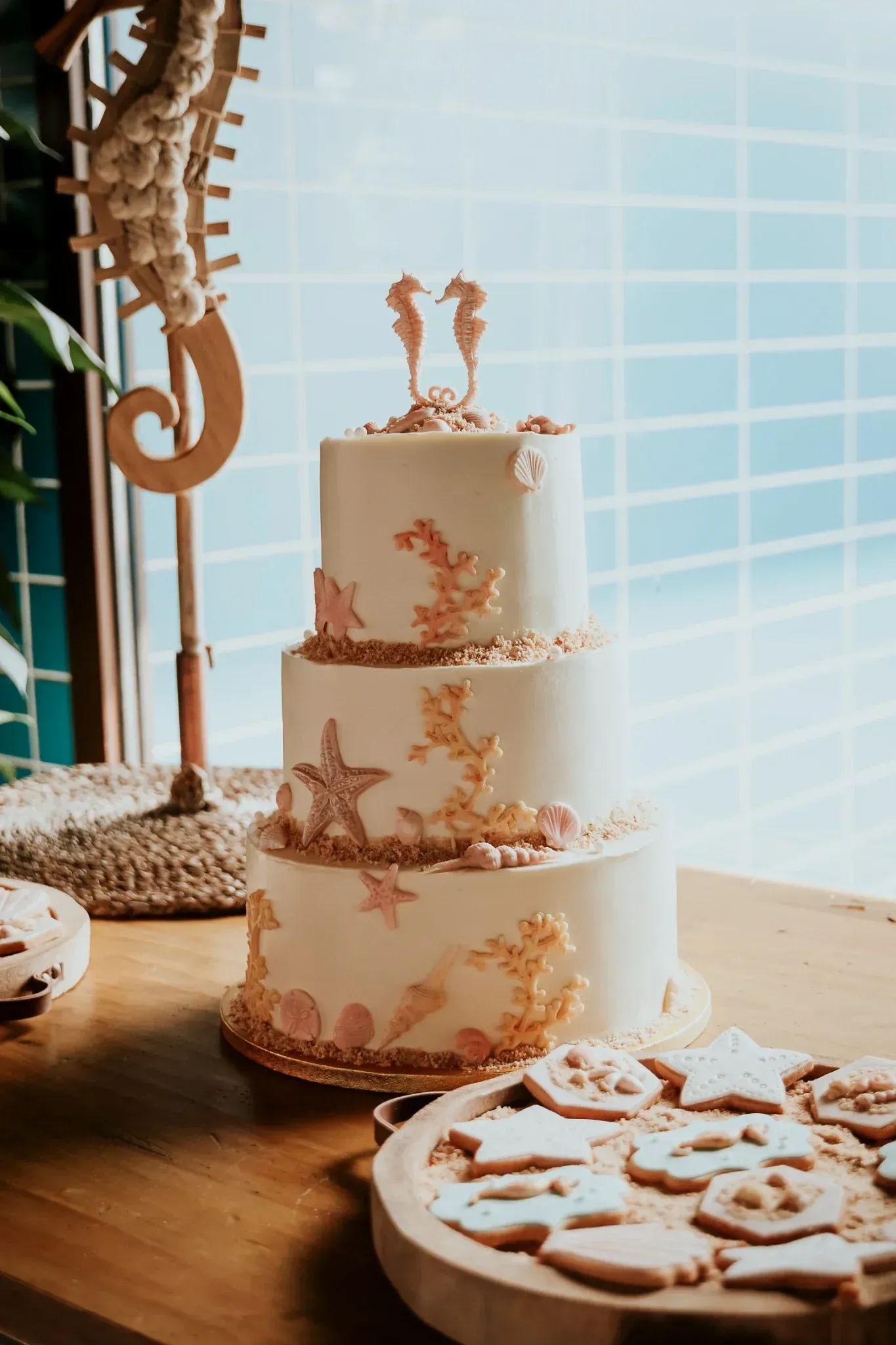 Pastel de bodas de tres niveles con decoraciones de coral y estrellas de mar, coronado con figuras de caballitos de mar