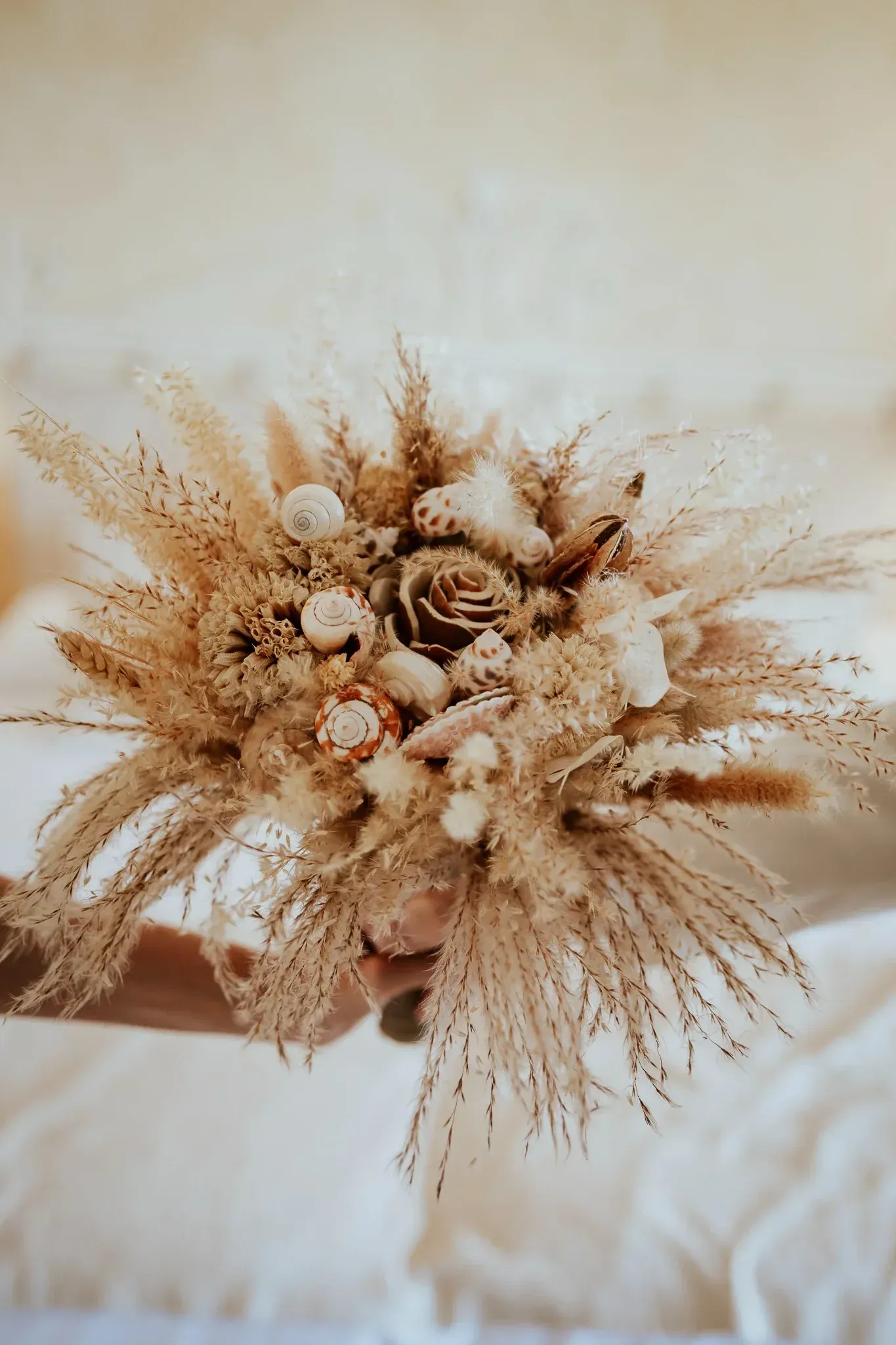 Primer plano de una mano sosteniendo un ramo de flores secas con una paleta de colores crema y beige.
