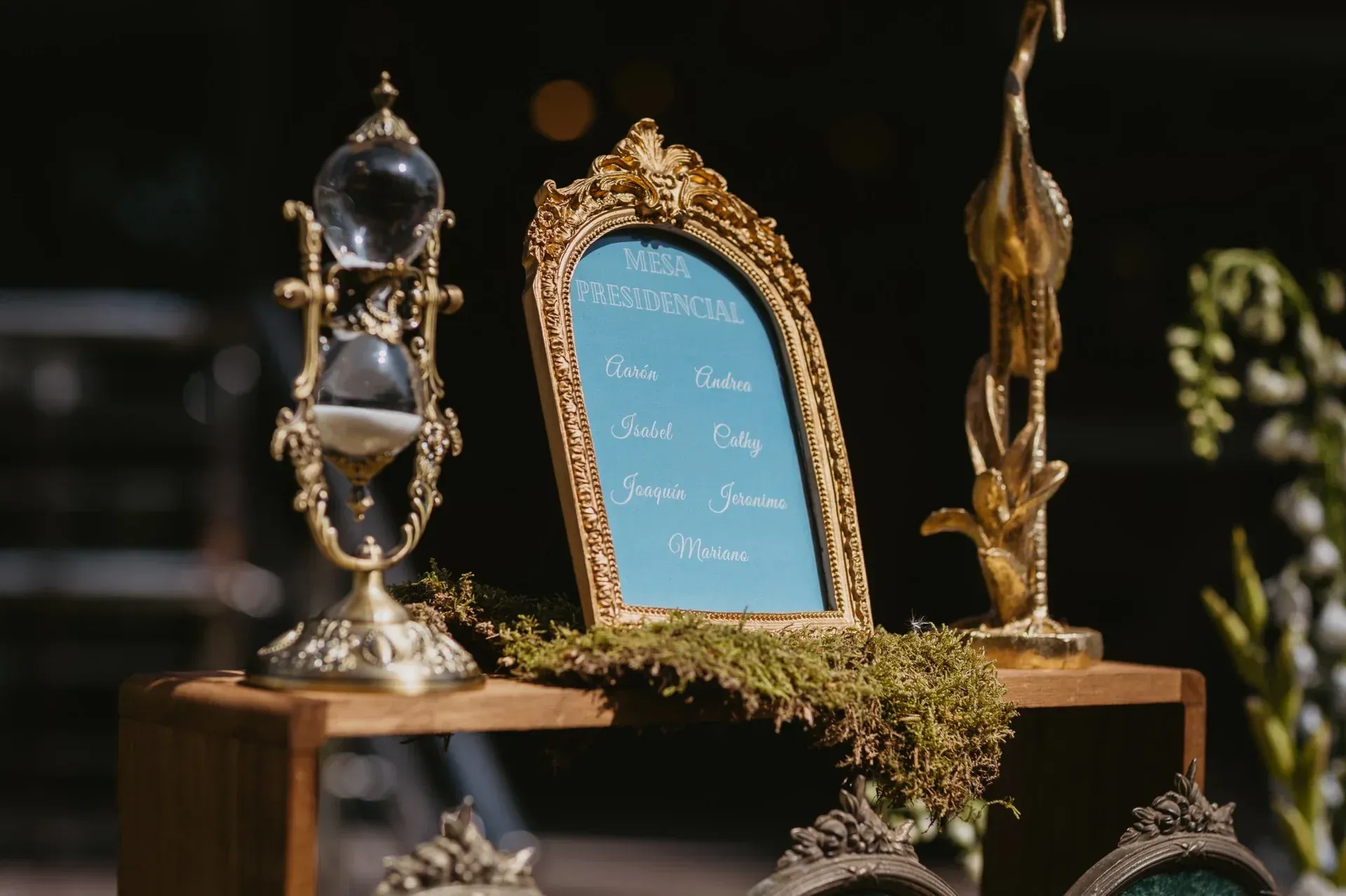 Plano de asientos con marco dorado sobre soporte de madera. Un reloj de arena y una escultura dorada lo flanquean