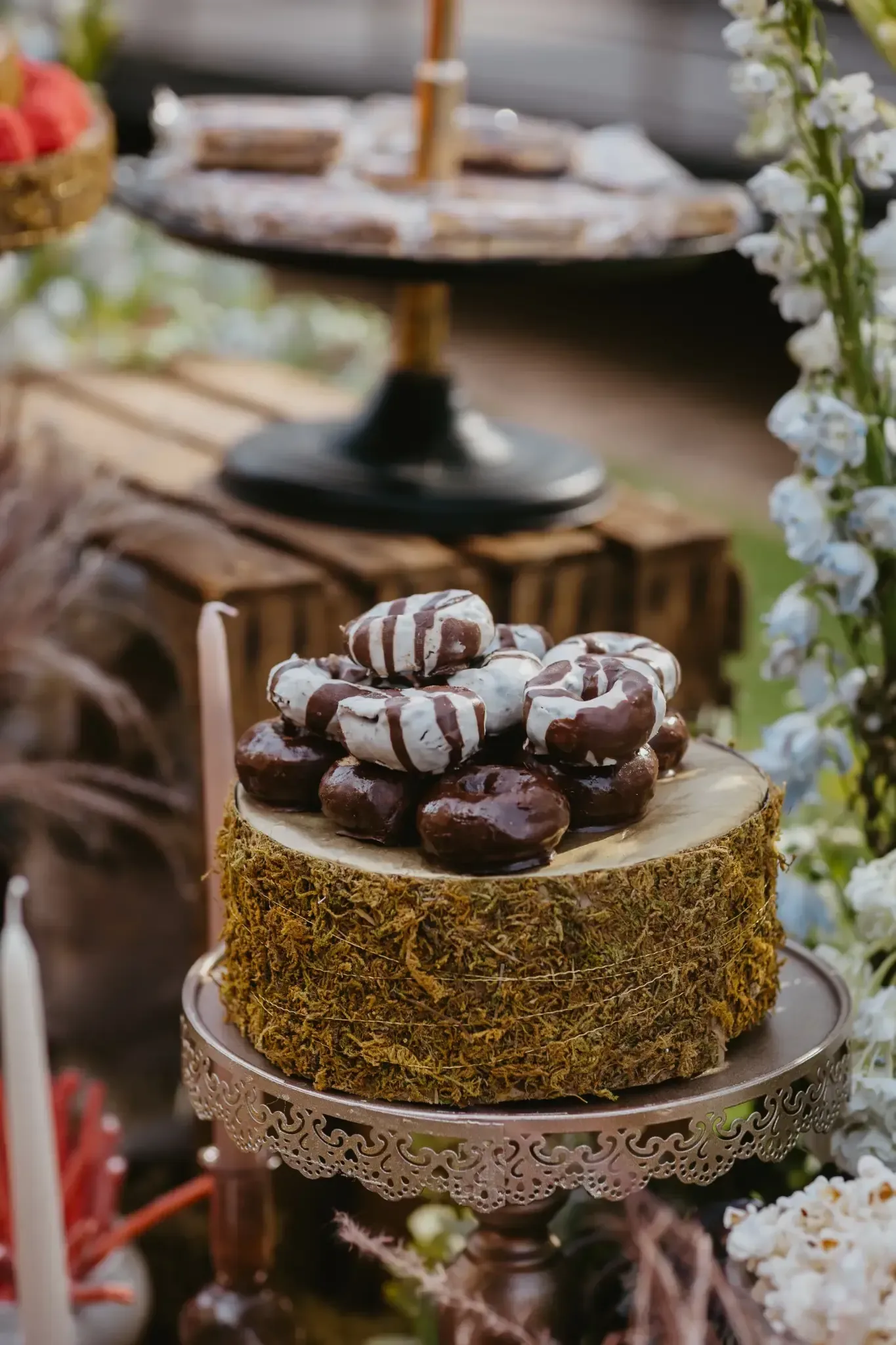 Exhibición de postres: Donas de chocolate y glaseadas apiladas sobre un soporte de oro y madera.