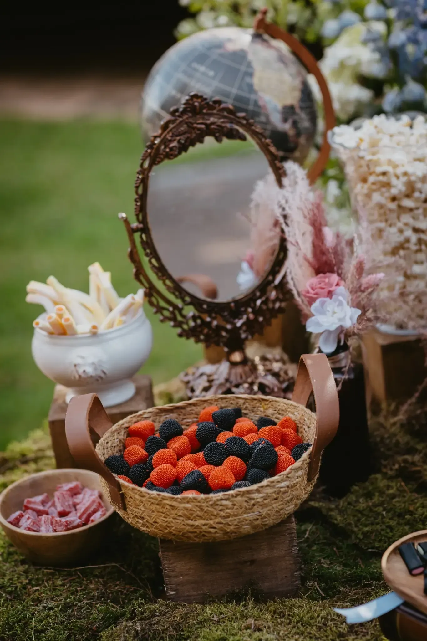 Una mesa decorativa con un espejo, bocadillos que incluyen bayas y palitos de pan, y un globo terráqueo
