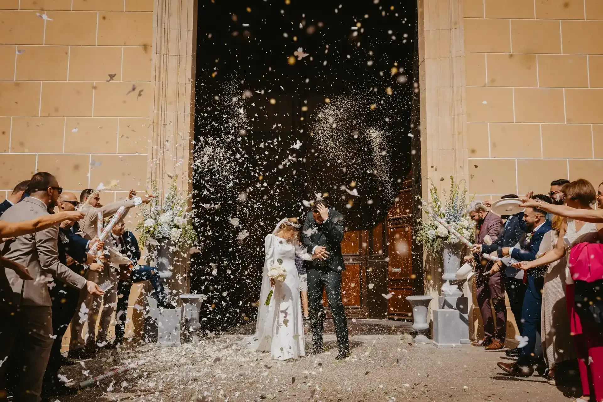 Los recién casados ​​salen de una iglesia, cubiertos de confeti, rodeados de invitados.