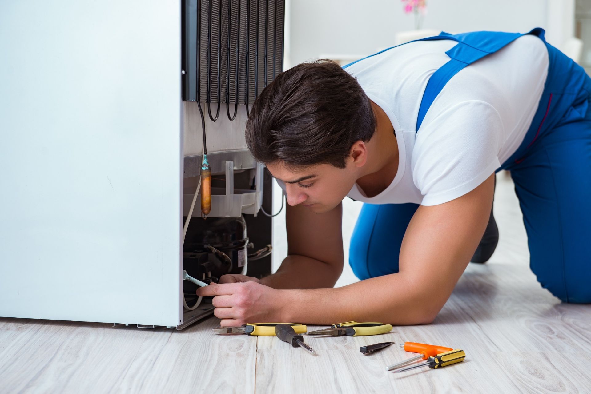 Un hombre está arrodillado en el suelo arreglando un refrigerador.