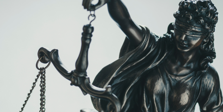 Gros plan sur une statue de la Justice, représentée avec un bandeau sur les yeux et tenant une balance. La statue est en métal sombre, probablement en bronze.