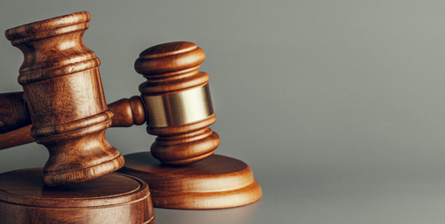 Deux maillets de juge en bois sur fond gris. L’un est posé debout sur sa base, l’autre est couché sur le côté.