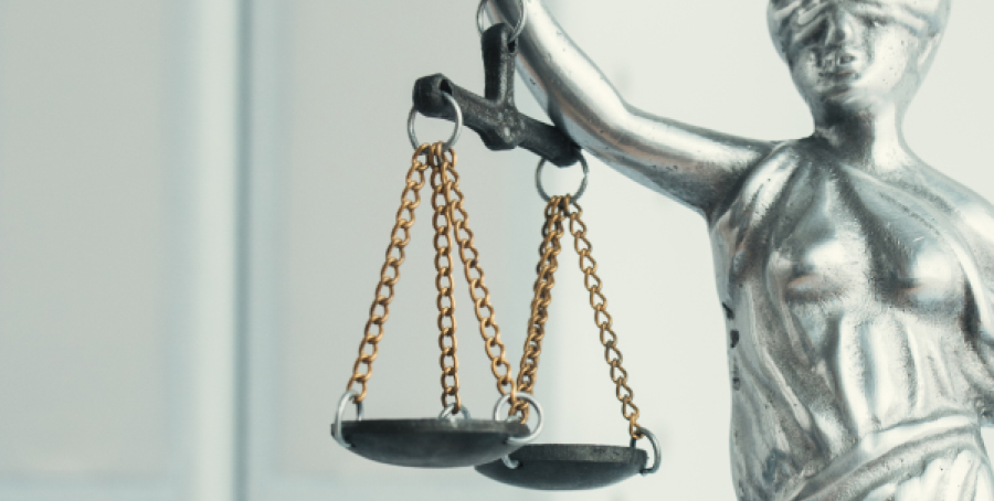 Statue de la Justice en gros plan, mettant en avant les balances suspendues par des chaînes, tenues dans sa main. La statue est métallique.