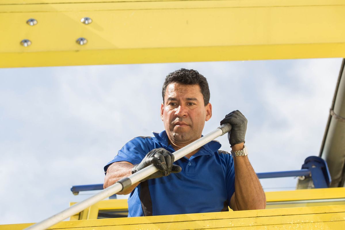 Mann in blauem Hemd und Handschuhen, der eine Stange hält, blickt nach oben unter ein gelbes Bauwerk.