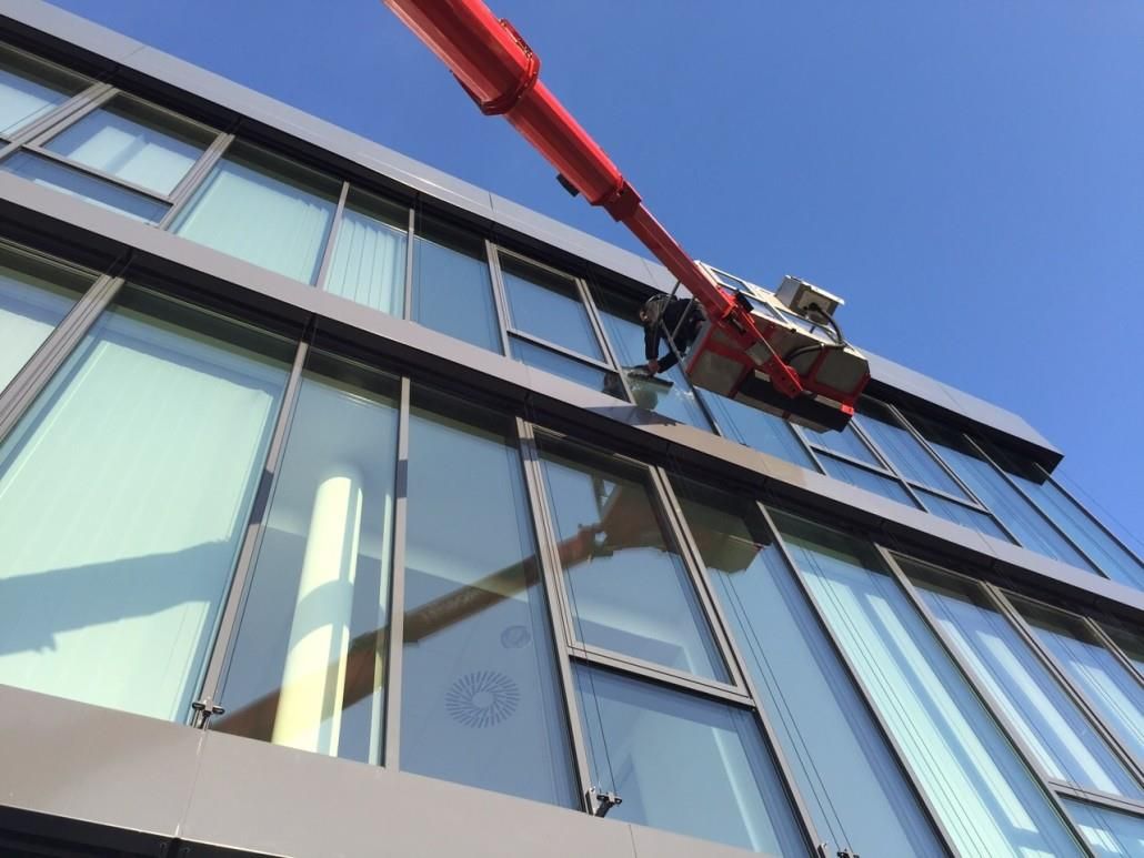 Roter Kran putzt Fenster an einem modernen Gebäude mit Glasplatten, klarer blauer Himmel.