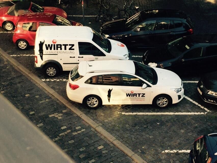 Weißer Lieferwagen und Auto mit „WIRTZ“-Logo zwischen anderen Fahrzeugen geparkt.