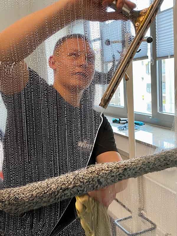 Mann reinigt ein Fenster mit einem Abzieher und Seifenwasser.