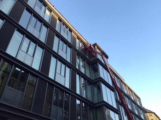 Roter Aufzug, der in ein modernes Gebäude mit vielen Fenstern vor blauem Himmel führt.