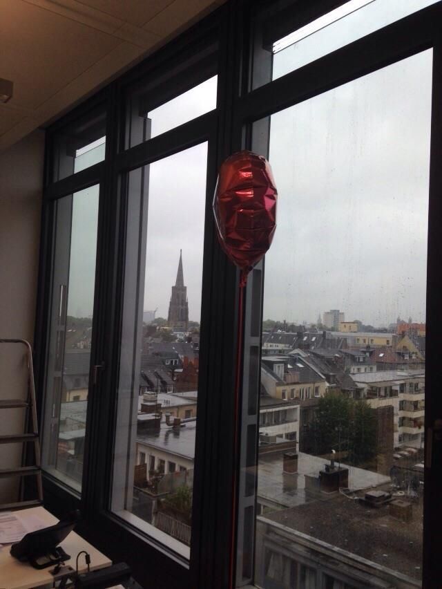 Roter Ballon neben einem Fenster mit Blick auf die Stadtlandschaft an einem bewölkten Tag.