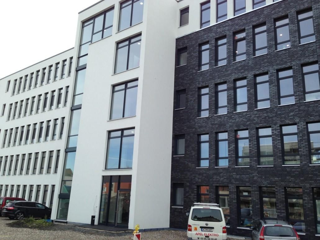 Modernes Bürogebäude mit weißer und dunkler Ziegelfassade, Fenstern und in der Nähe geparkten Autos.