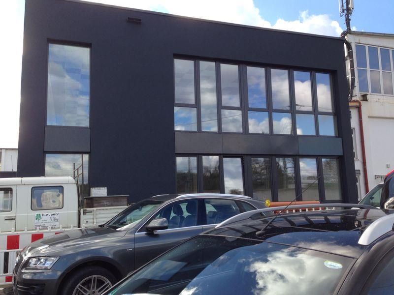 Modernes schwarzes Gebäude mit großen Fenstern; davor parkende Autos.