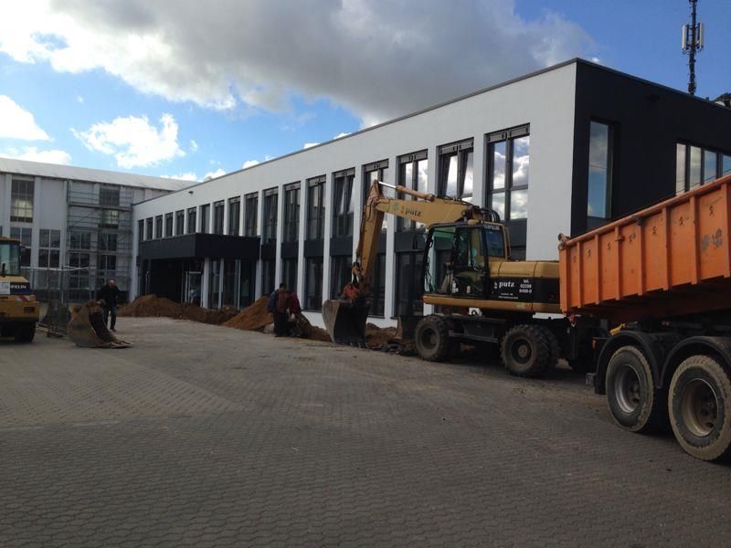 Baustelle mit Bagger, Muldenkipper und Arbeitern, die in der Nähe eines modernen Gebäudes graben.