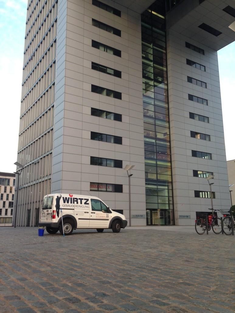 Ein modernes, hohes Gebäude, vor dem ein weißer Servicewagen geparkt ist.