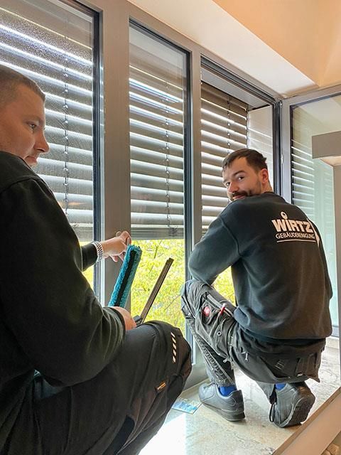 Zwei Fensterputzer, einer putzt ein Fenster, der andere schaut zurück. Sie sind drinnen.