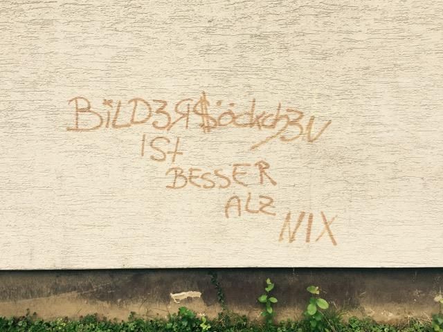 Brown graffiti on a white wall reads 